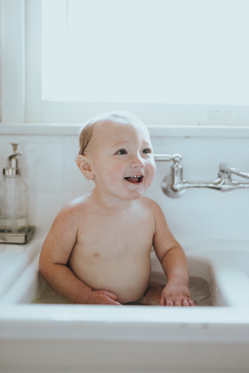 topless baby lying on white ceramic bathtub